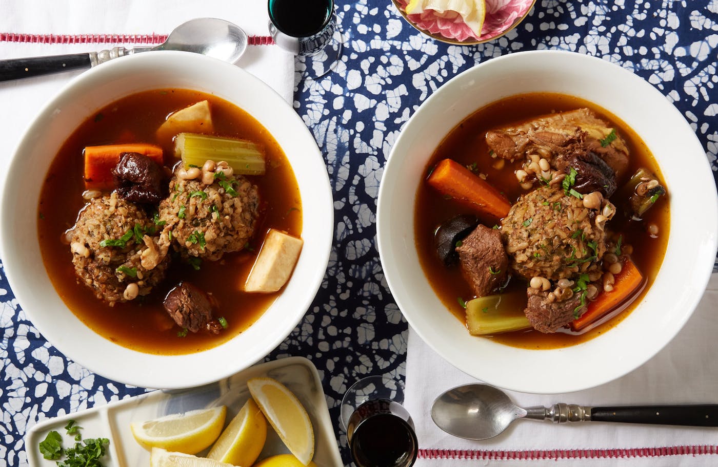 Persian meatball soup with fresh parsley alongside dishes of lemon wedges and parsley, atop blue speckles tablecloth.