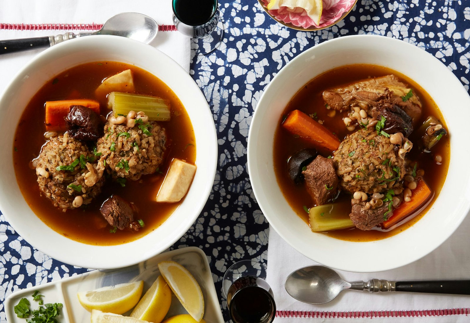 Persian meatball soup with fresh parsley alongside dishes of lemon wedges and parsley, atop blue speckles tablecloth.