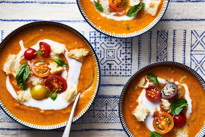 Three bowls of soup atop blue and white tablecloth.