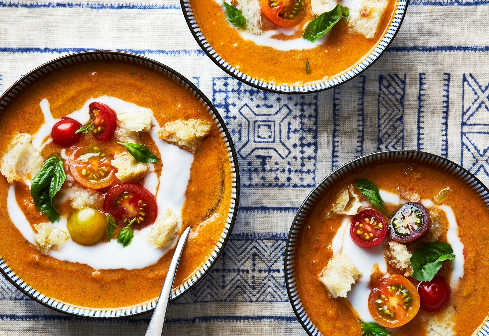Three bowls of soup atop blue and white tablecloth.