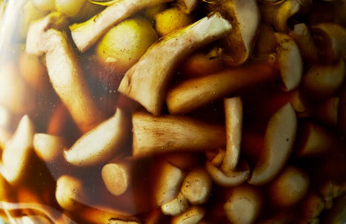Closeup pickling jar with mushrooms in brown brine.