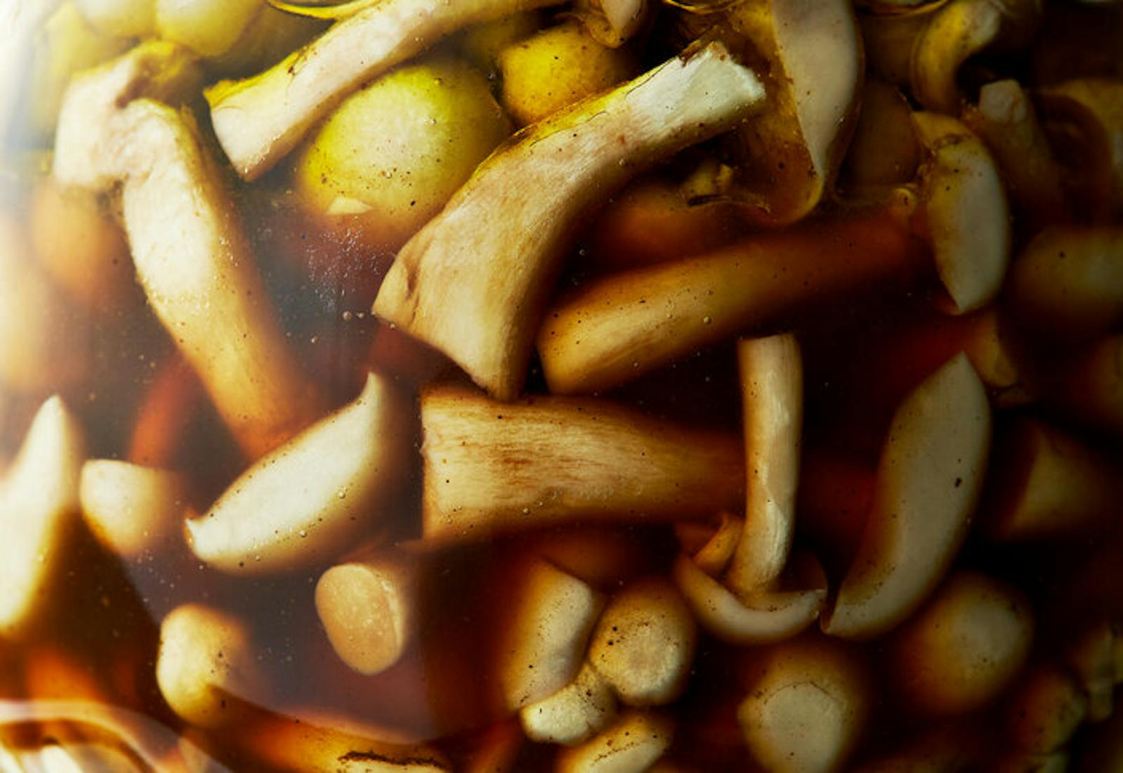 Closeup pickling jar with mushrooms in brown brine.