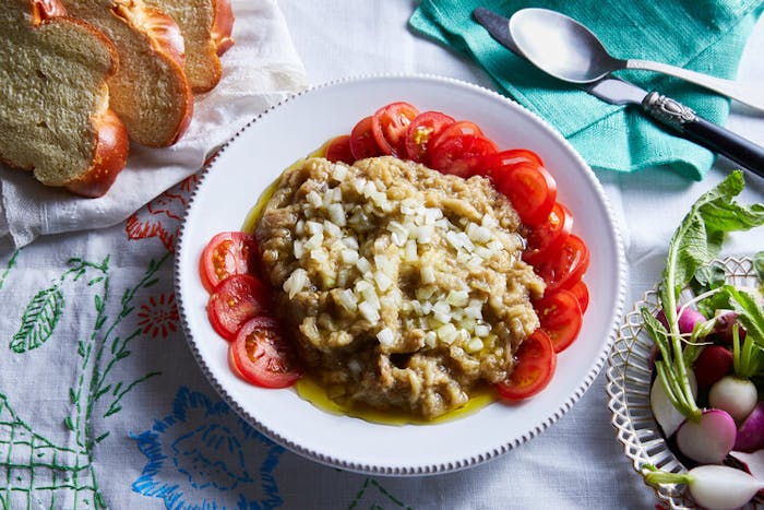 Eggplant salad with raw onions and tomatoes alongside sliced challah and bowl of halved radishes.