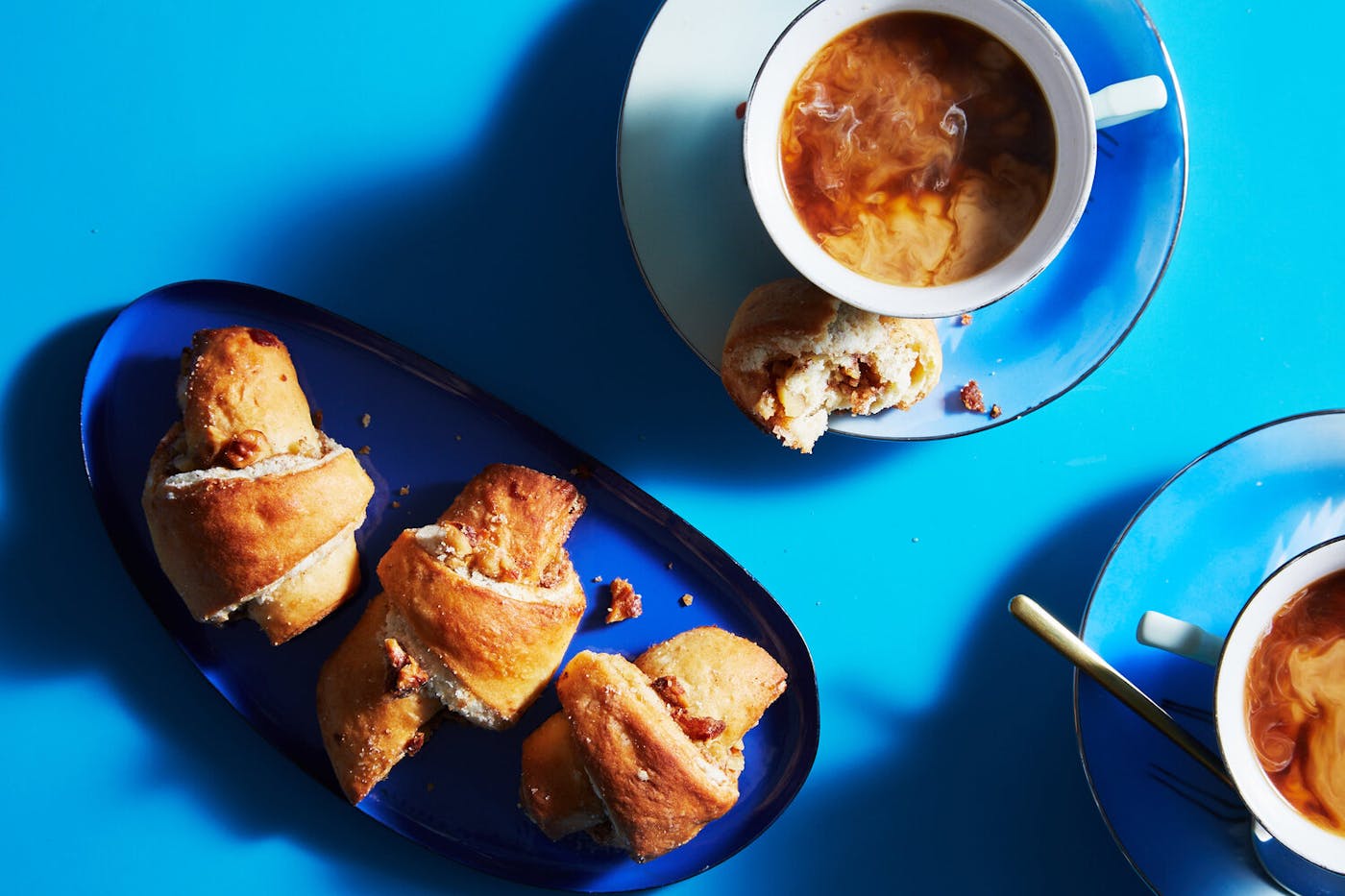 Butter horns on blue plates with mugs of milky coffee.