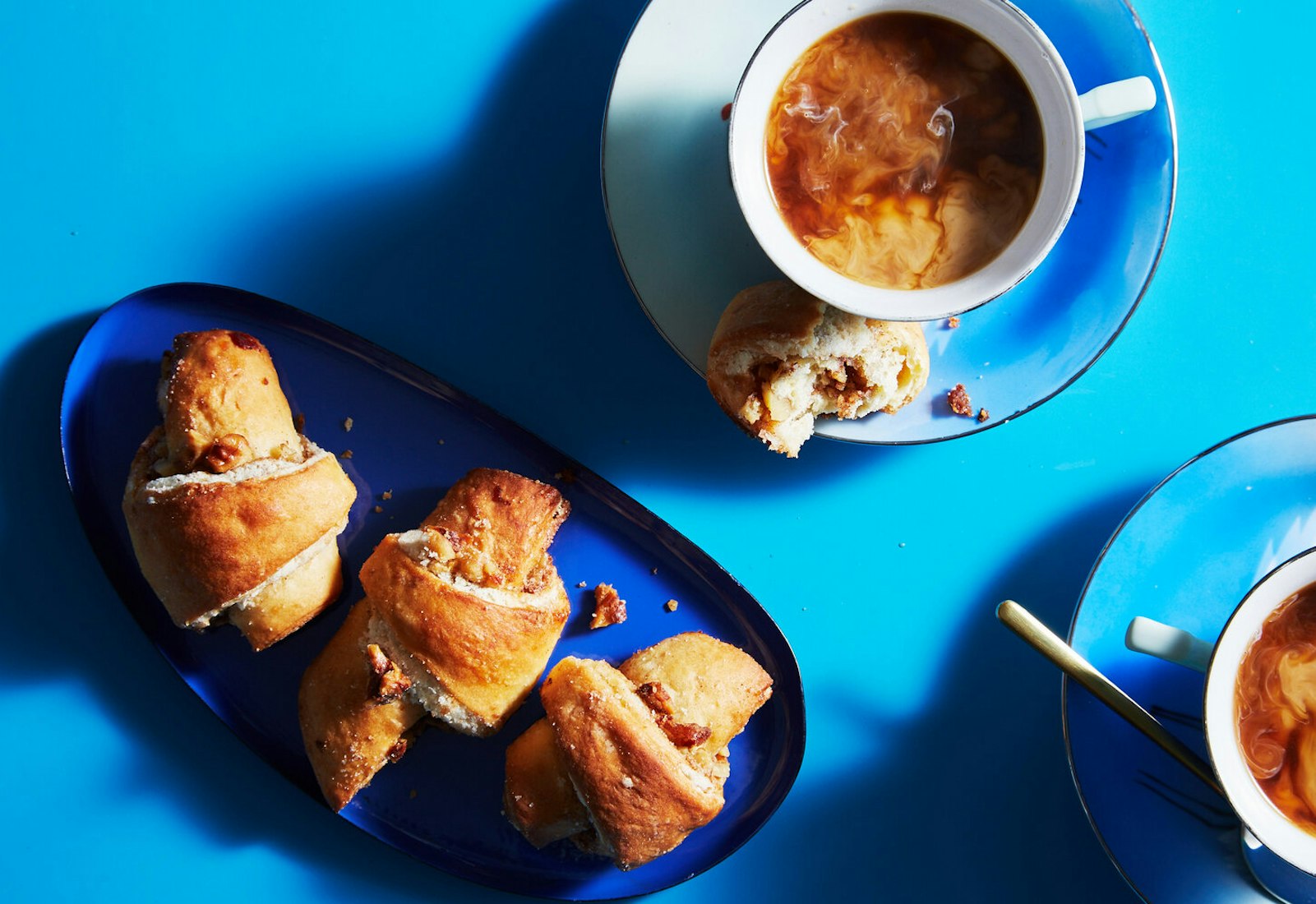 Butter horns on blue plates with mugs of milky coffee.