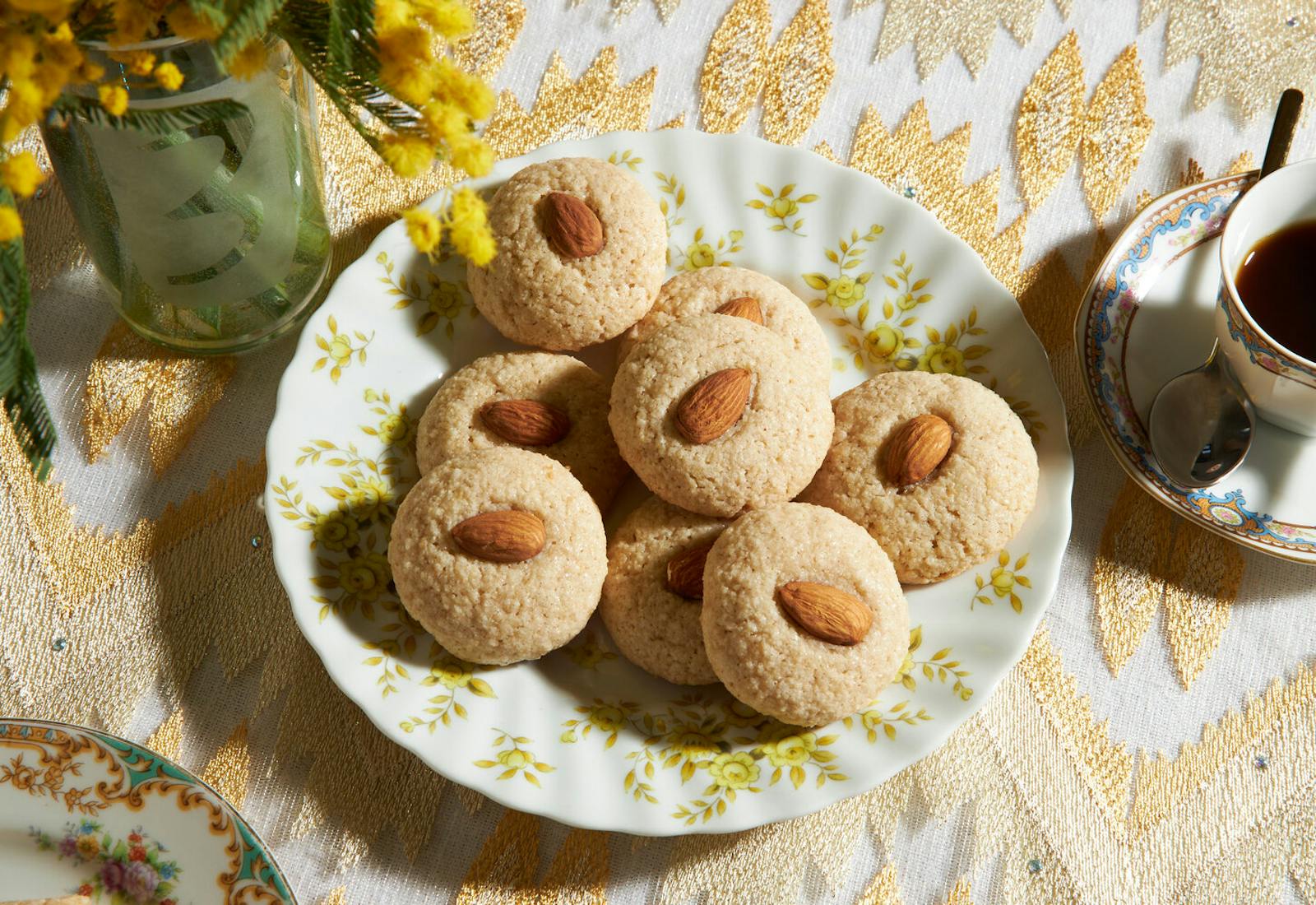 Cookies on yellow floral plate with tea and fresh flowers, atop gold tablecloth.