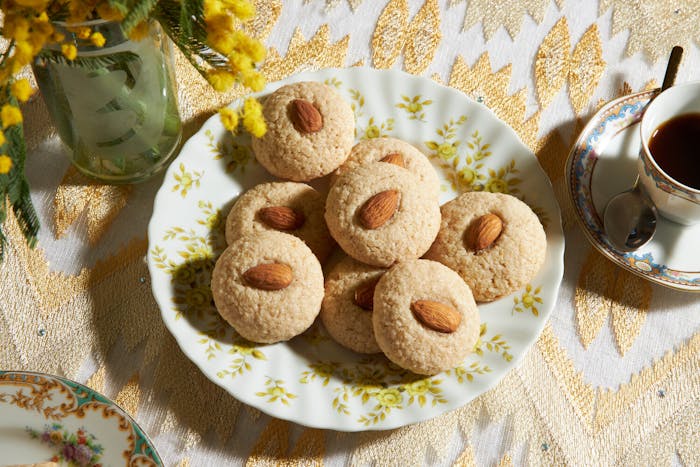 Cookies on yellow floral plate with tea and fresh flowers, atop gold tablecloth.