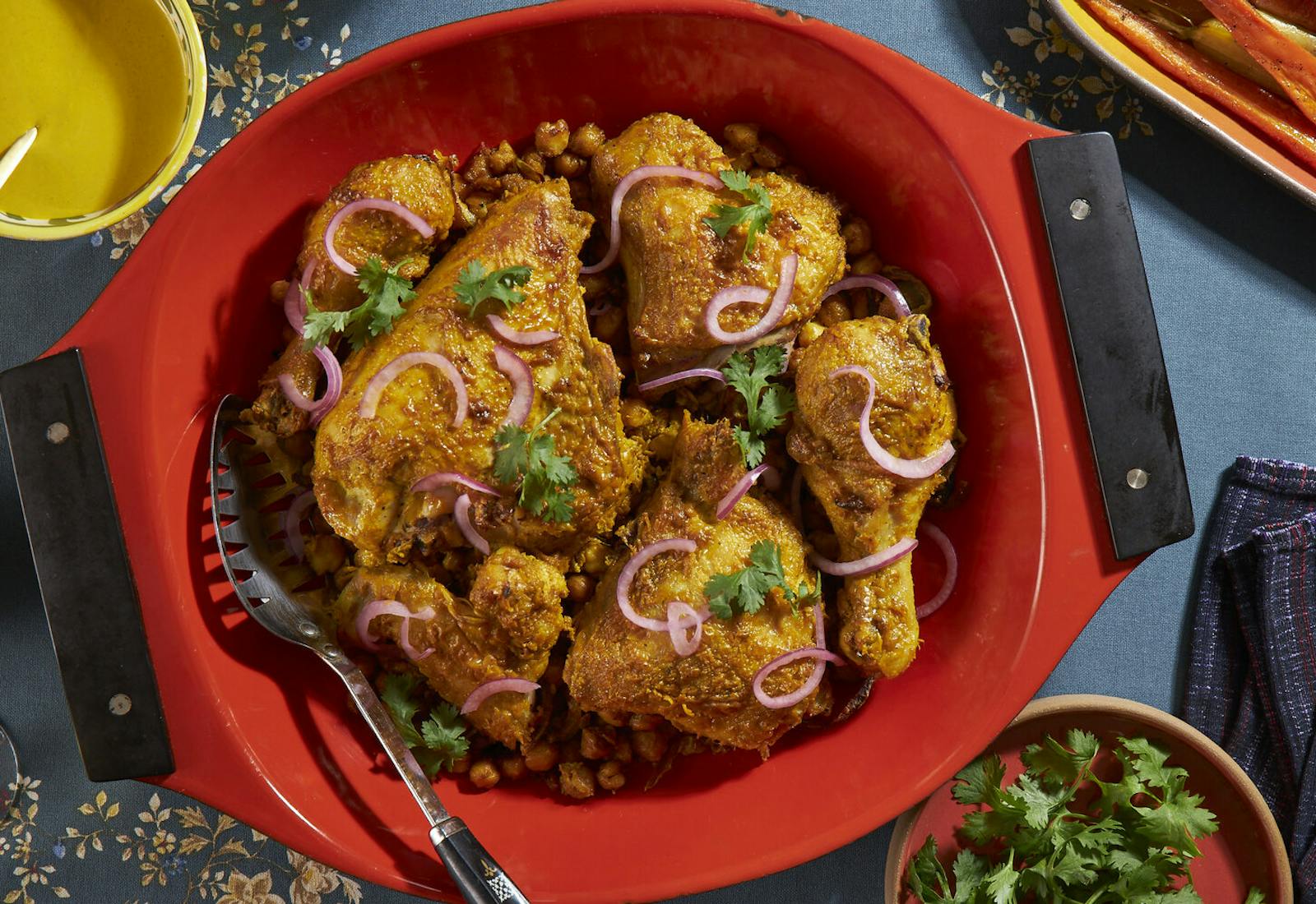 Chicken garnished with red onions and cilantro and turmeric tahini sauce atop blue tablecloth.