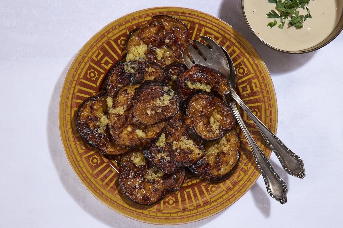 Fried eggplant slices sprinkled with garlic and cumin, side of tahini with parsley.