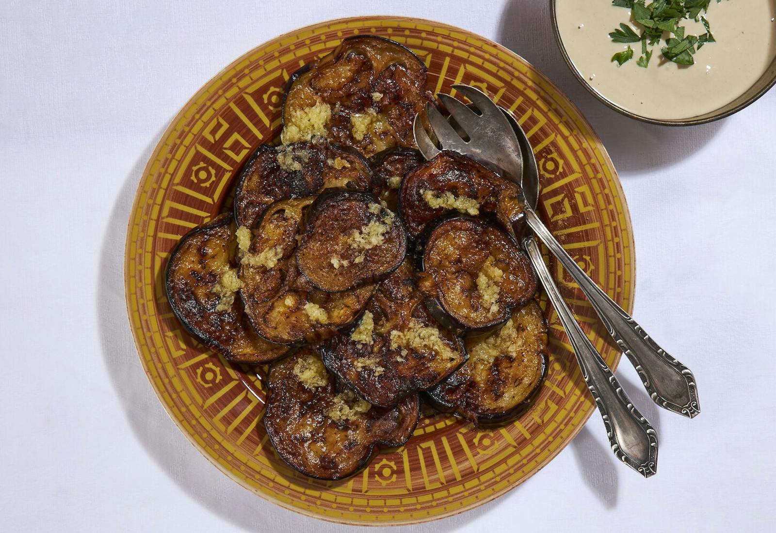 Fried eggplant slices sprinkled with garlic and cumin, side of tahini with parsley.