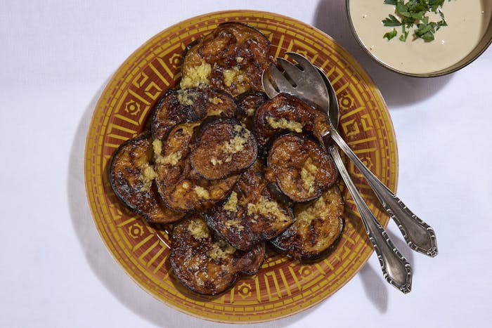 Fried eggplant slices sprinkled with garlic and cumin, side of tahini with parsley.