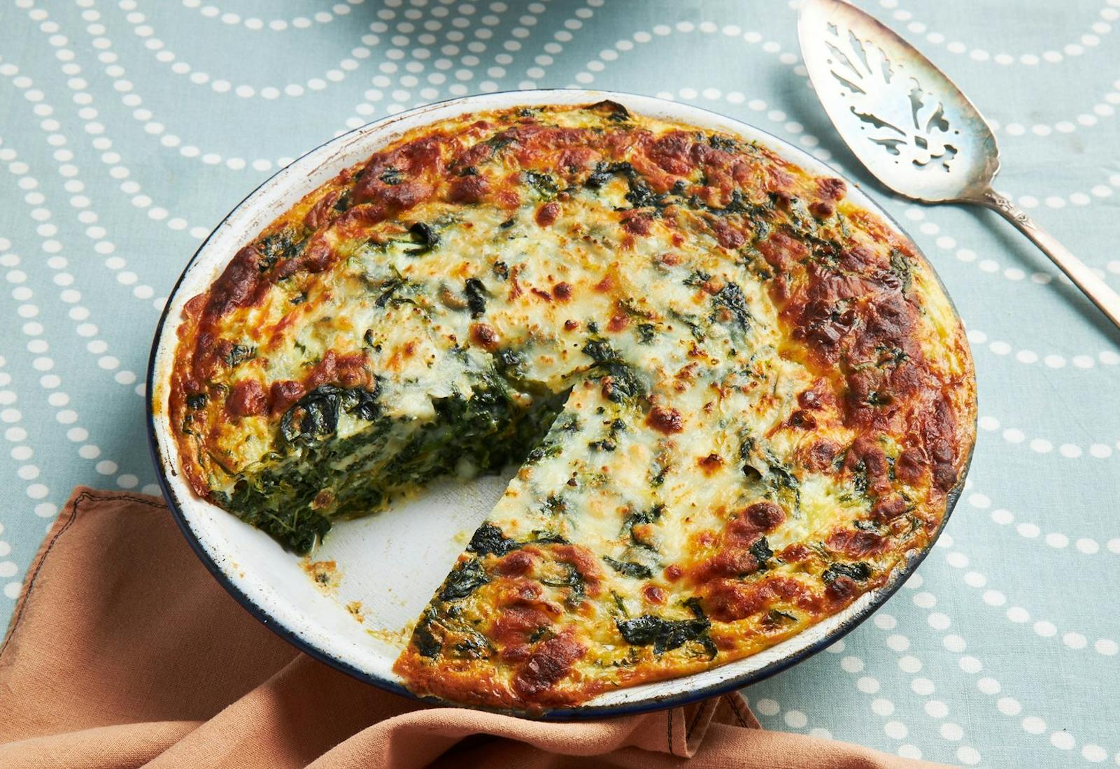 Spinach and cheese jibon in white dish atop blue tablecloth.