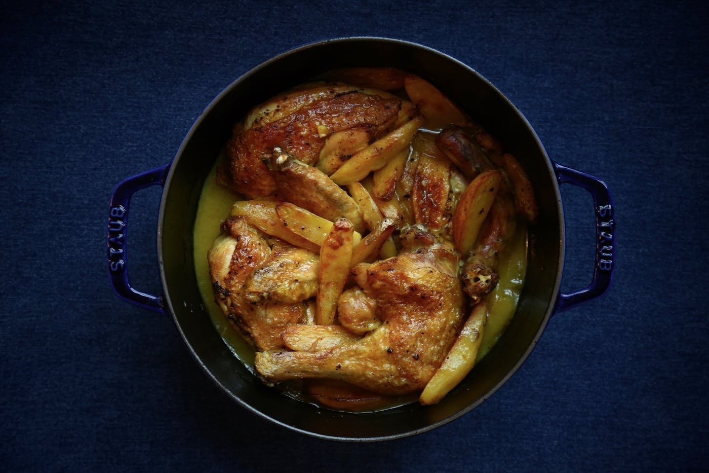 Egyptian chicken sofrito in navy cast iron pot atop blue surface. 