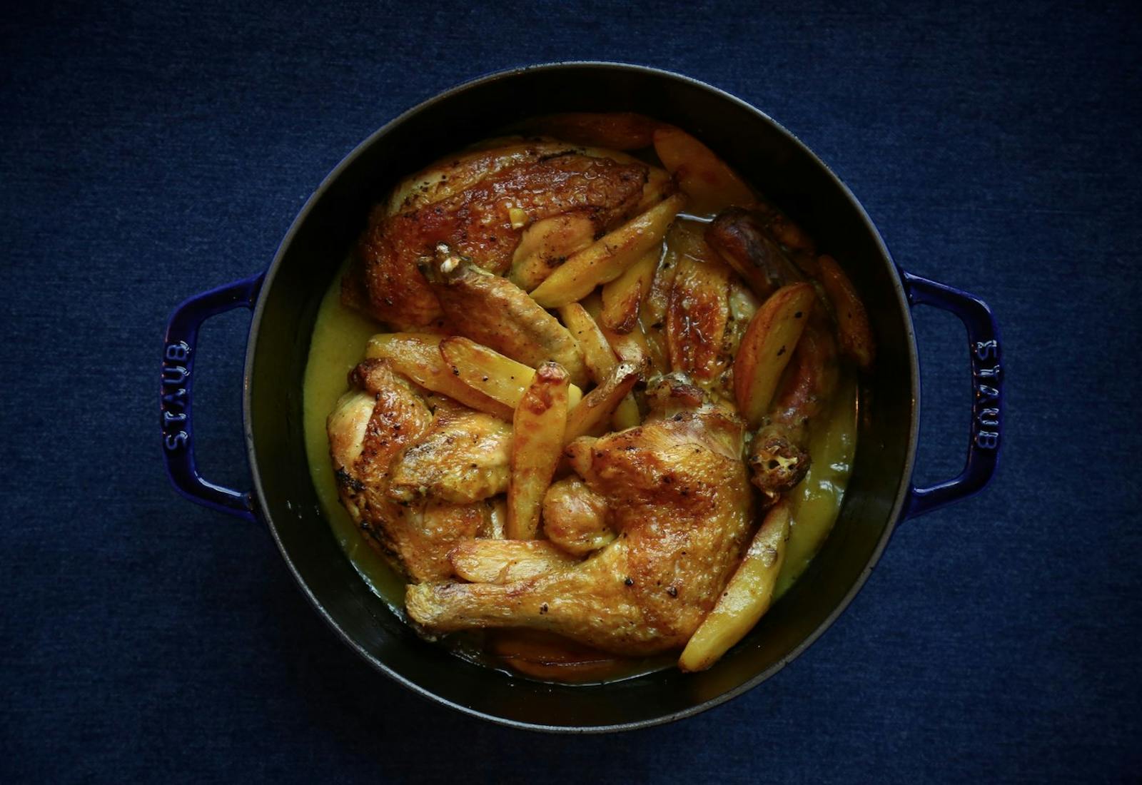 Egyptian chicken sofrito in navy cast iron pot atop blue surface. 