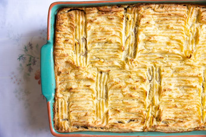 Baked pastela in blue casserole dish atop white floral tablecloth.