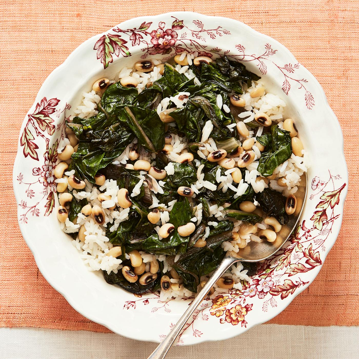 Rice with black eyed peas and chard in white floral bowl over salmon tablecloth.