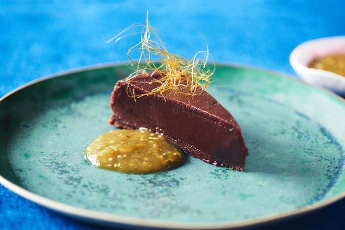 Slice of boca negra with dollop of tomatillo sauce on blue plate atop blue tablecloth.