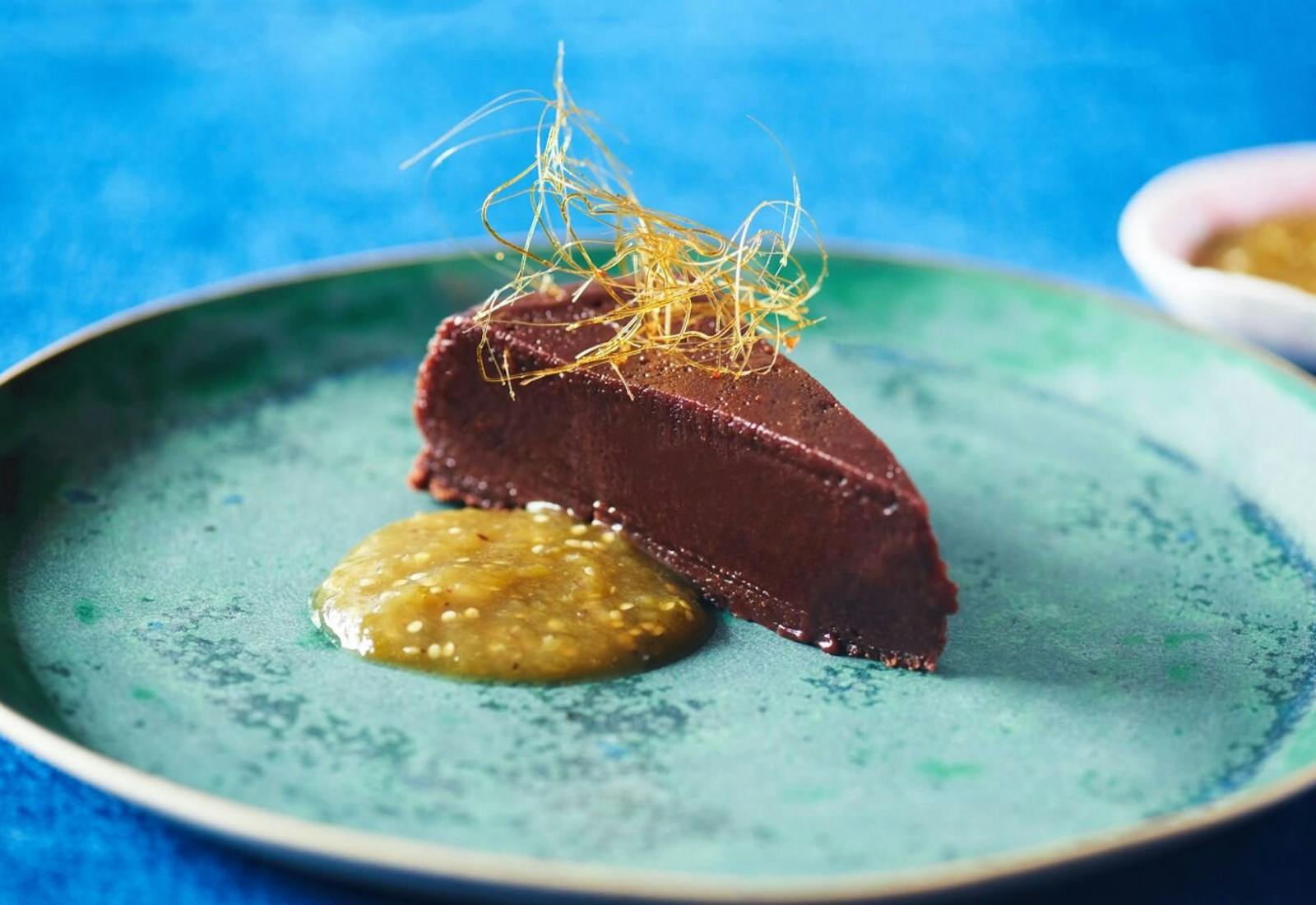 Slice of boca negra with dollop of tomatillo sauce on blue plate atop blue tablecloth.