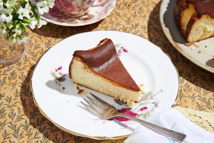 Burnished cheesecake with tea cups, serving plate, and white flowers.