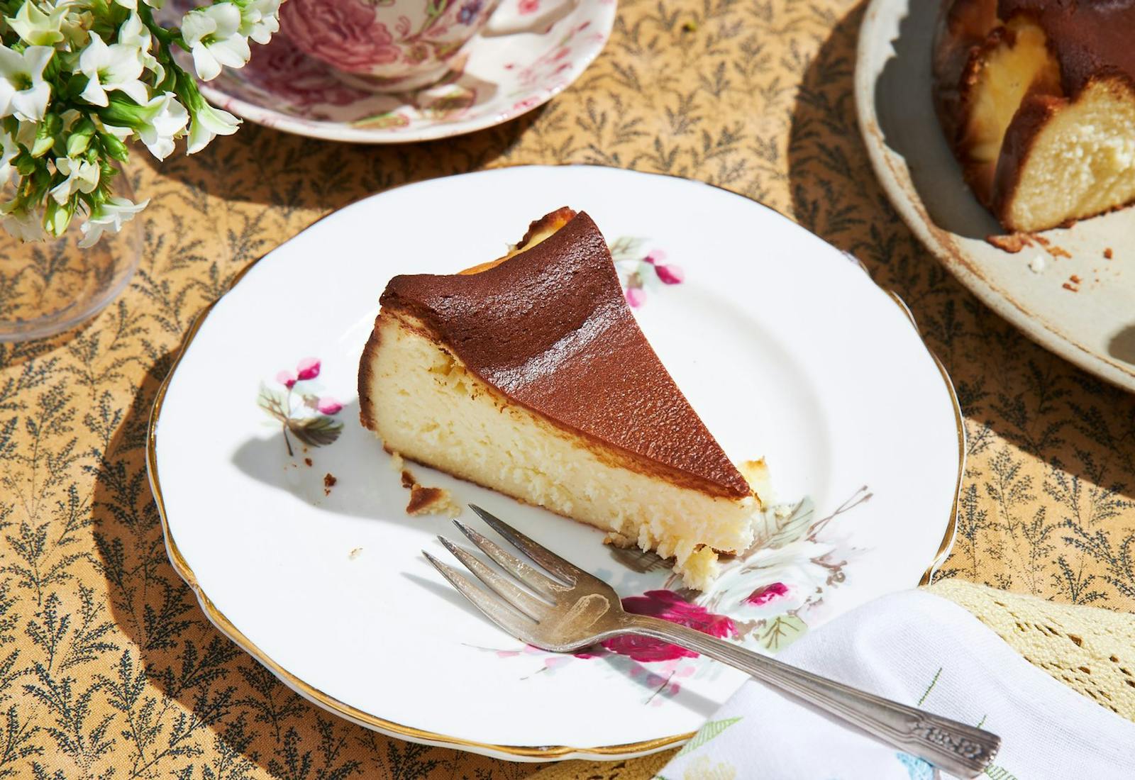 Burnished cheesecake with tea cups, serving plate, and white flowers.