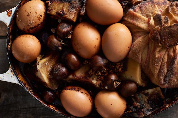 Coolant with baked eggs, chestnuts, beef bones and cheesecloth with rice in white cast iron dish.