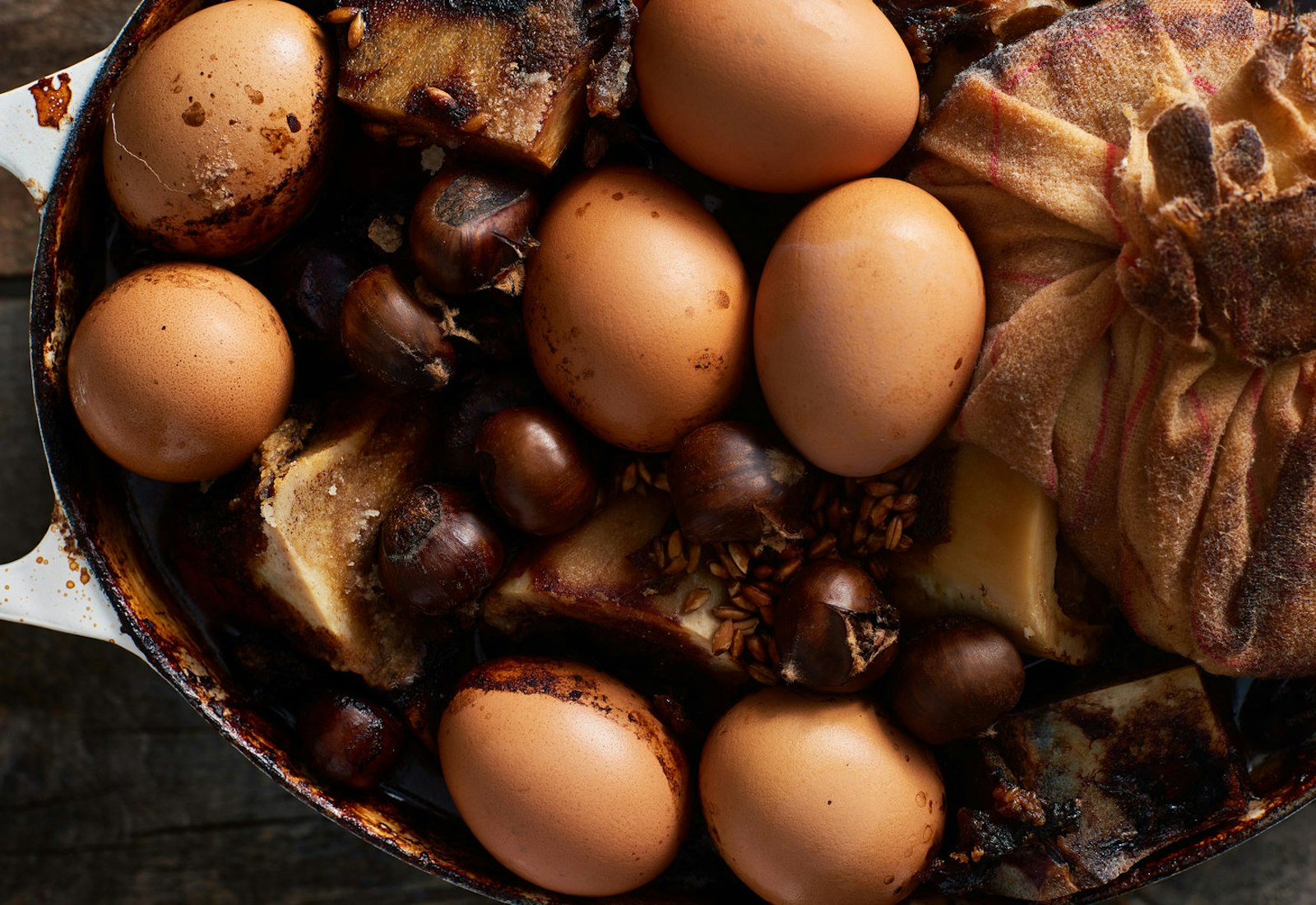 Coolant with baked eggs, chestnuts, beef bones and cheesecloth with rice in white cast iron dish.