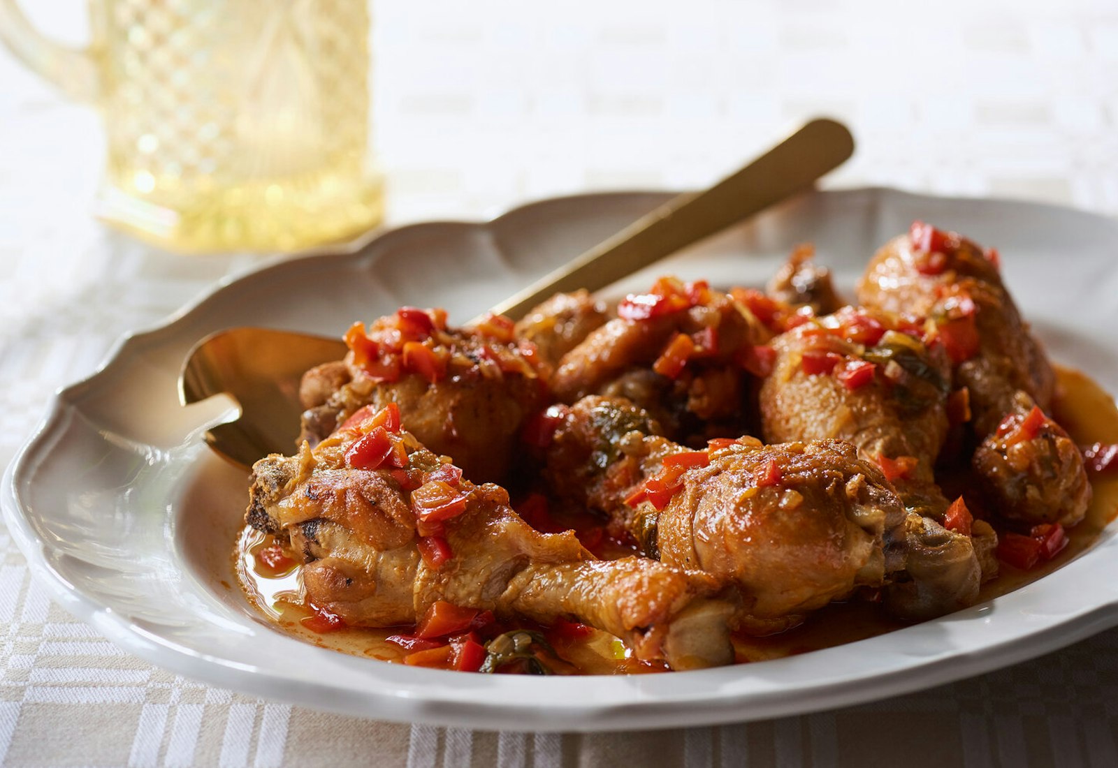 Chicken paprikash on white serving dish, gold serving fork atop tan and white tablecloth.