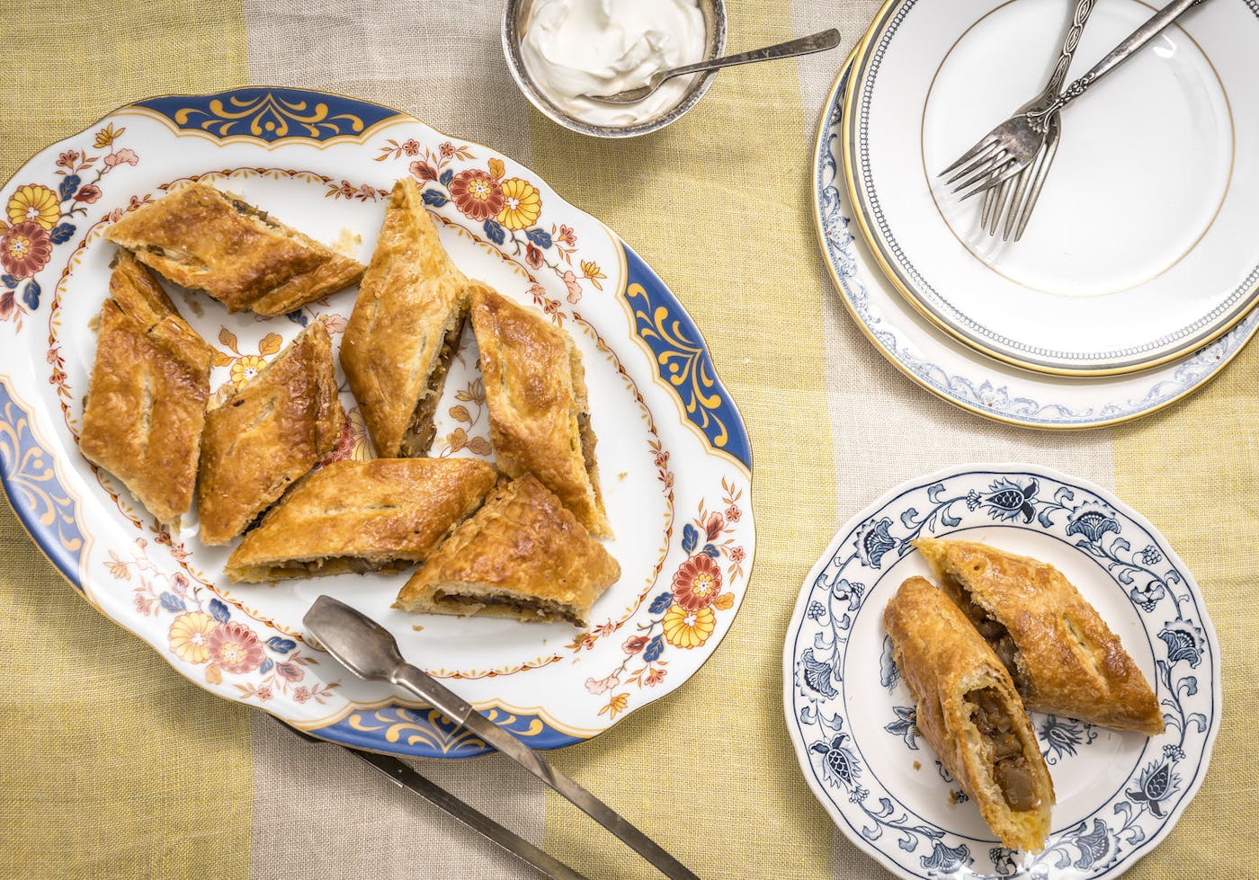 Sliced handrajo on floral plates with serving utensils alongside bowl of sour cream atop yellow striped tablecloth.