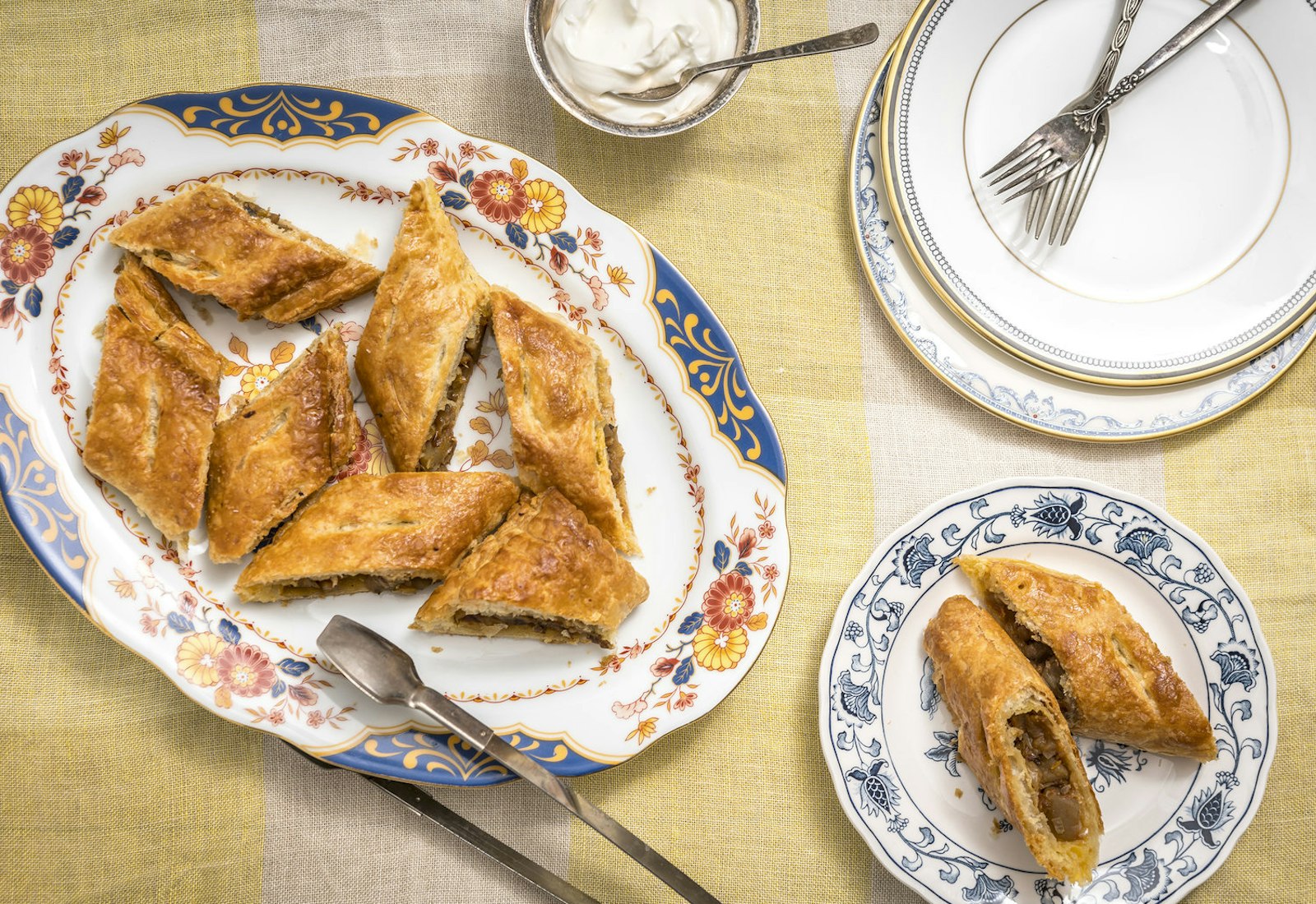 Sliced handrajo on floral plates with serving utensils alongside bowl of sour cream atop yellow striped tablecloth.
