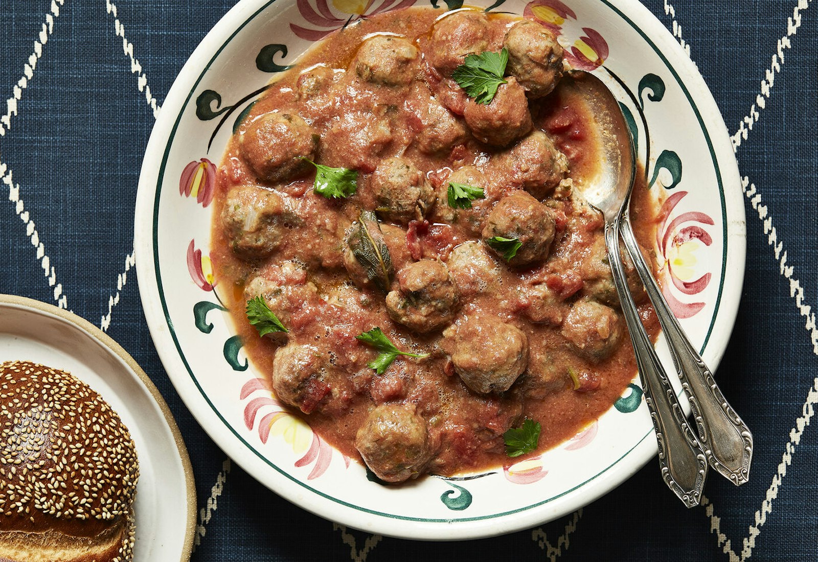 Meatballs in tomato sauce with parsley, seeded bread atop navy tablecloth.