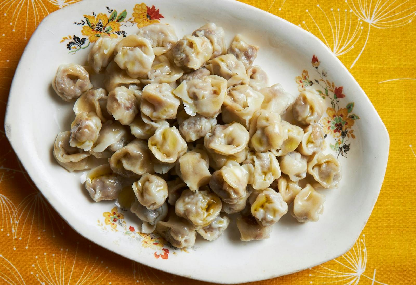 Pelmeni dumplings with a drizzle of olive oil, atop bright orange tablecloth.
