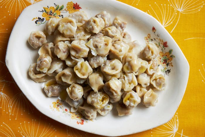 Pelmeni dumplings with a drizzle of olive oil, atop bright orange tablecloth.