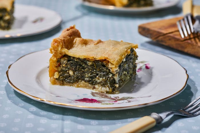 Slice of spanakopita on small dish, atop blue tablecloth.