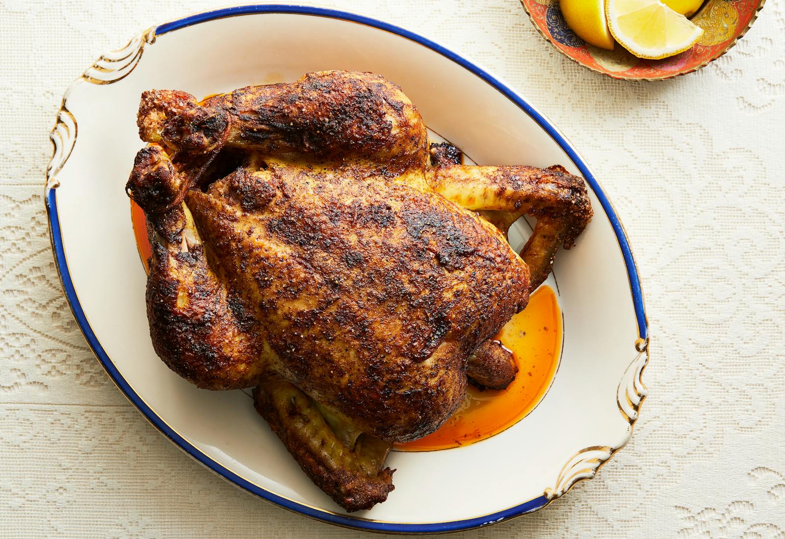 Roast chicken on oval serving platter atop white tablecloth.