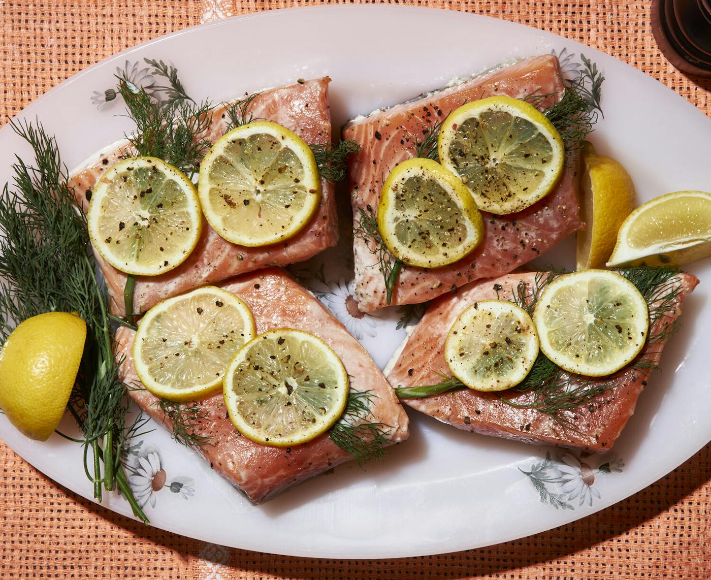 Poached salmon with sliced lemon and dill fronds on oval dish atop wicker surface.