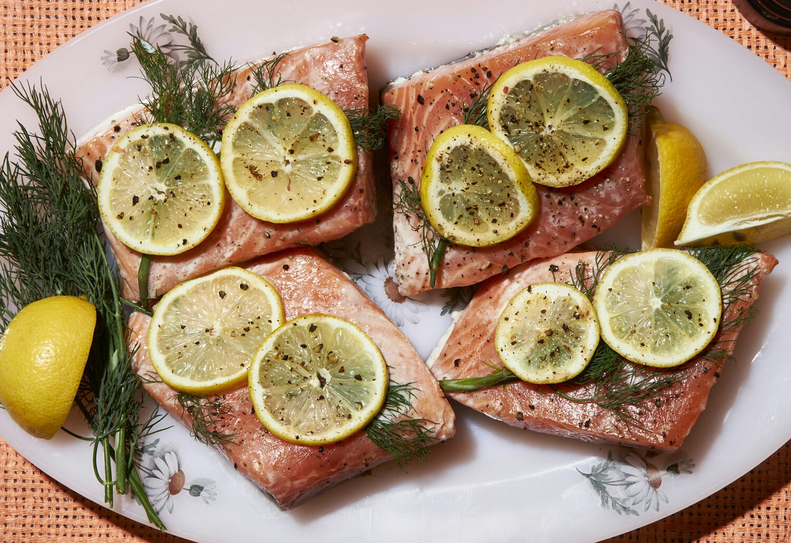 Poached salmon with sliced lemon and dill fronds on oval dish atop wicker surface.