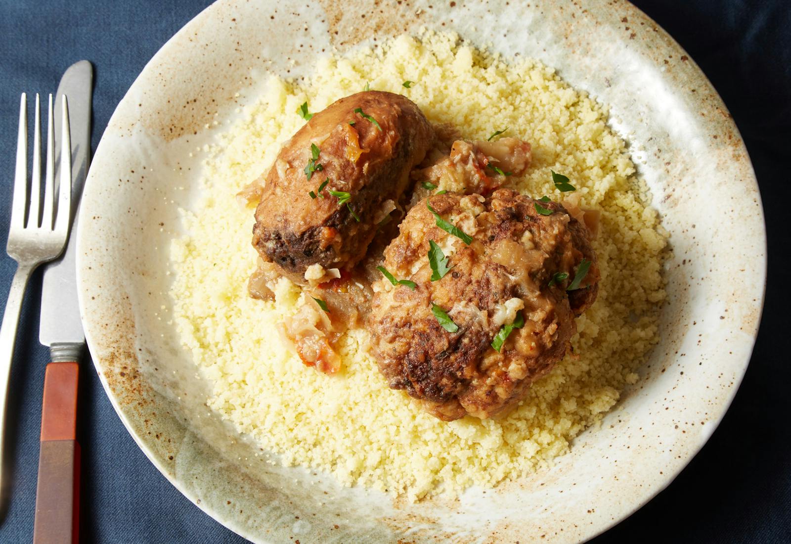 Mafrum garnished with cilantro over bed of couscous in tan speckled bowl atop dark blue tablecloth.