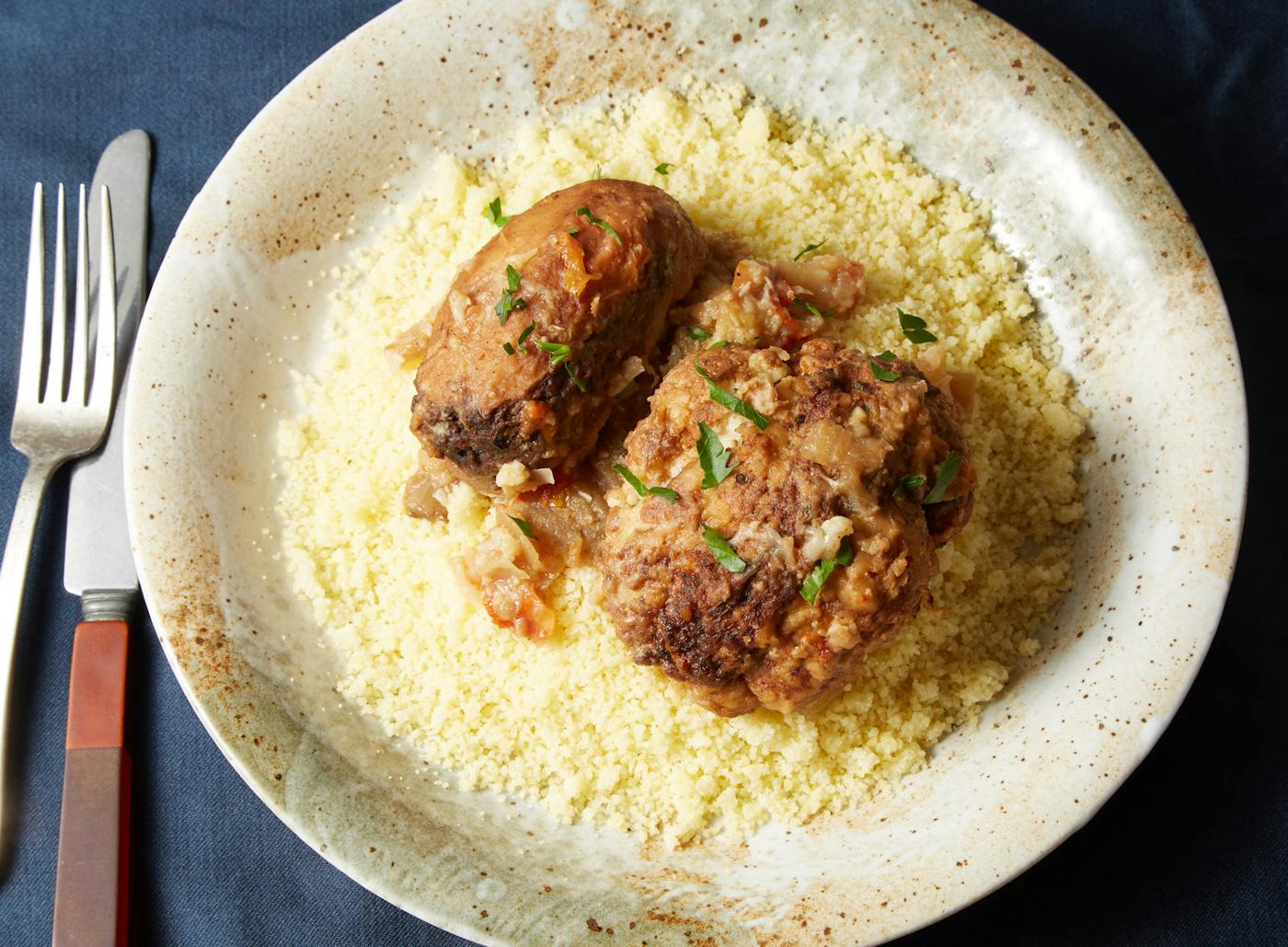 Mafrum garnished with cilantro over bed of couscous in tan speckled bowl atop dark blue tablecloth.