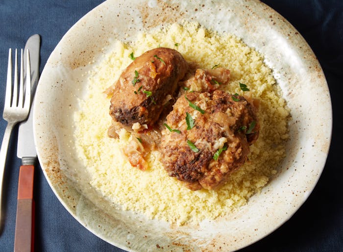 Mafrum garnished with cilantro over bed of couscous in tan speckled bowl atop dark blue tablecloth.