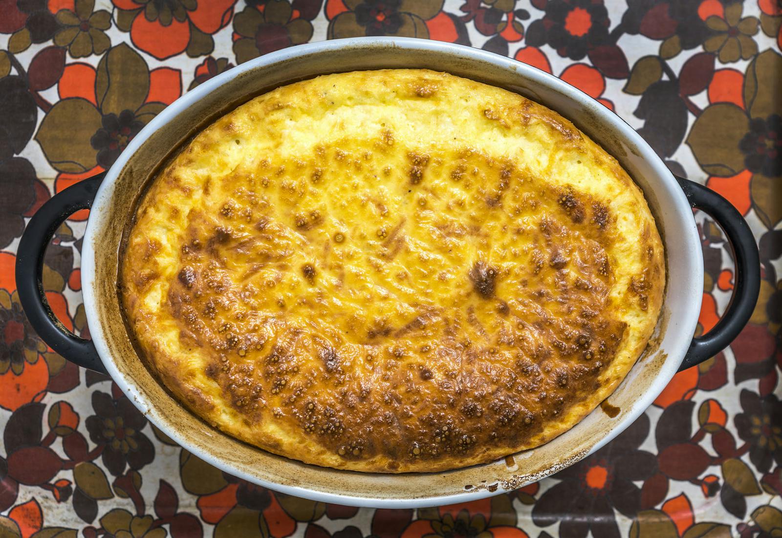 Golden dunce pie in black and white casserole dish atop red and brown floral tablecloth.