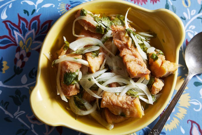 Escabeche with onion slices and cilantro in yellow bowl atop blue floral tablecloth.