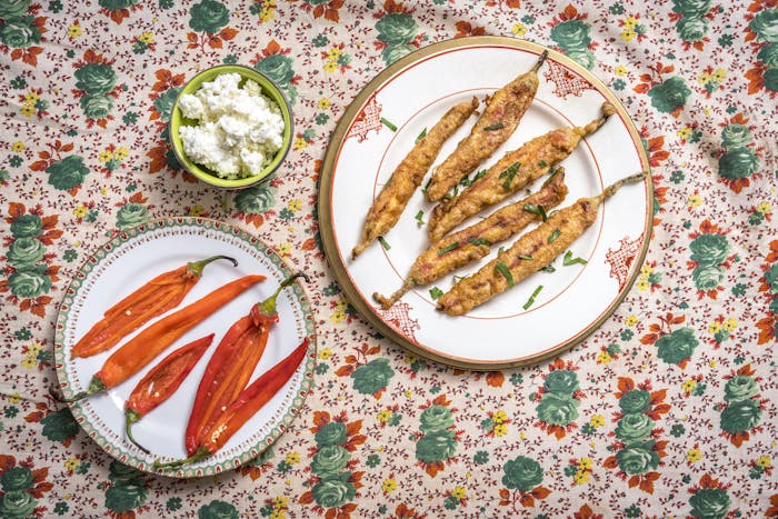 Fried chushki borek garnished with parsley alongside fresh peppers and cheese mix atop floral tablecloth.