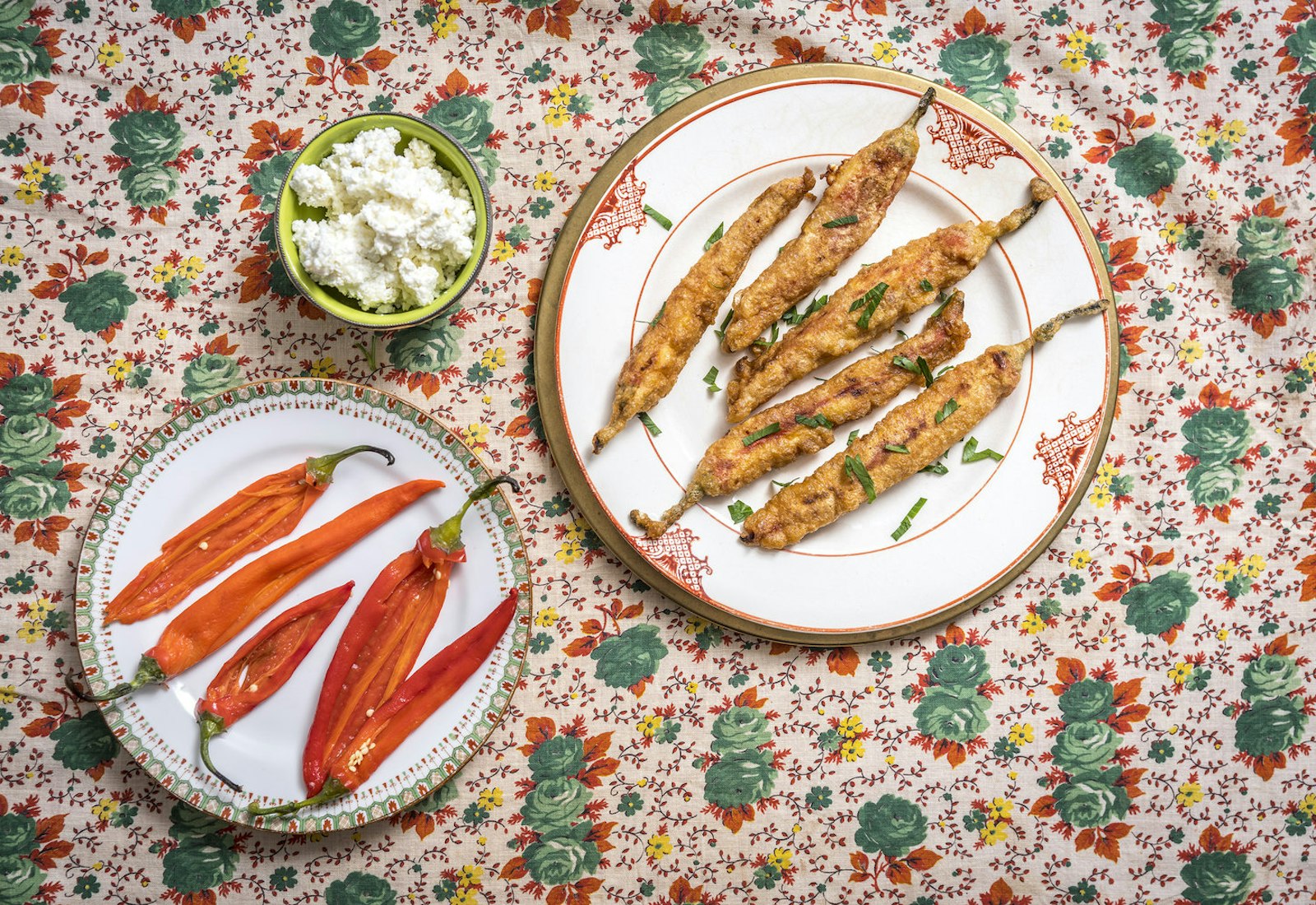Fried chushki borek garnished with parsley alongside fresh peppers and cheese mix atop floral tablecloth.