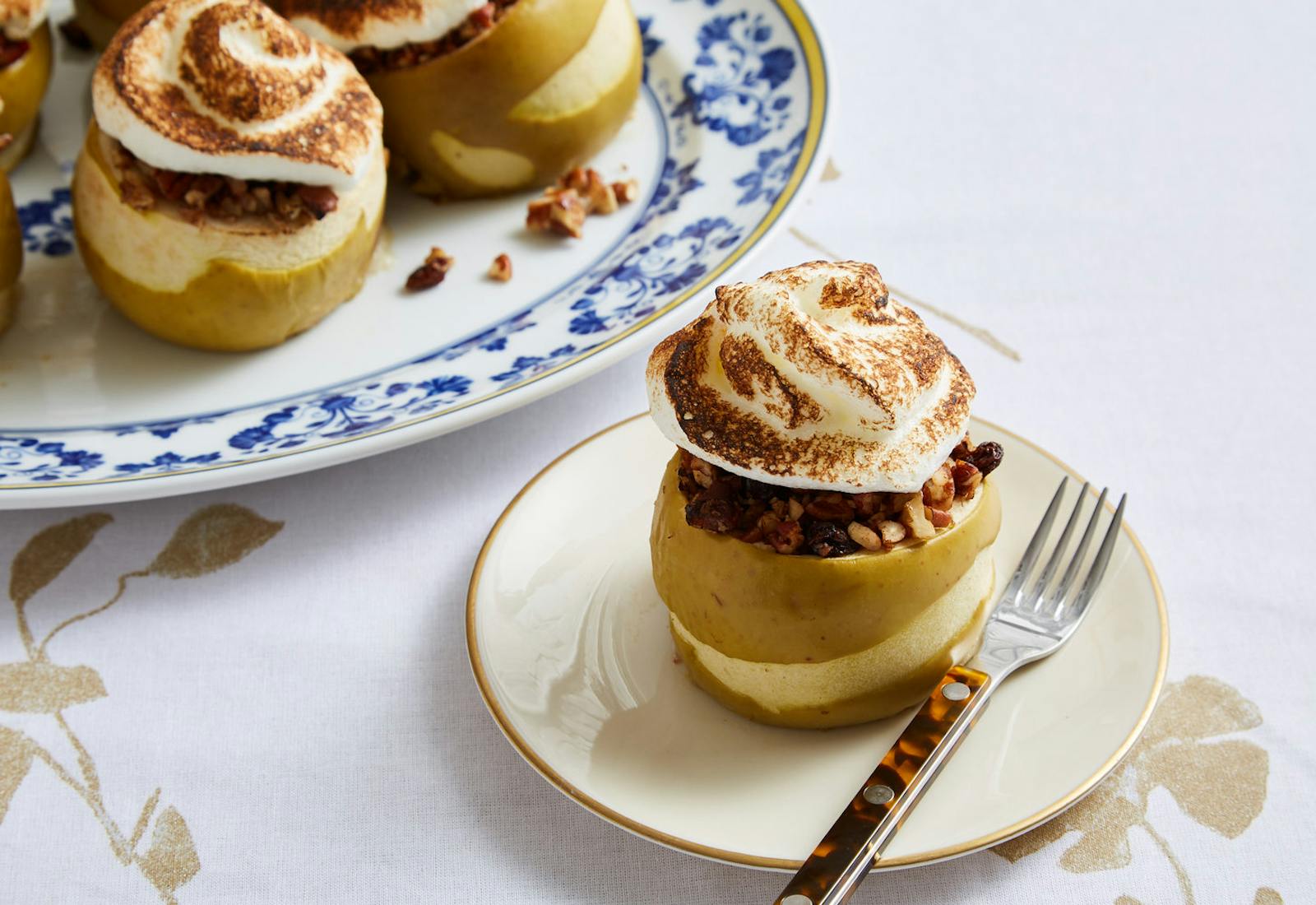 Baked apples with burnished meringue atop gold patterned tablecloth.