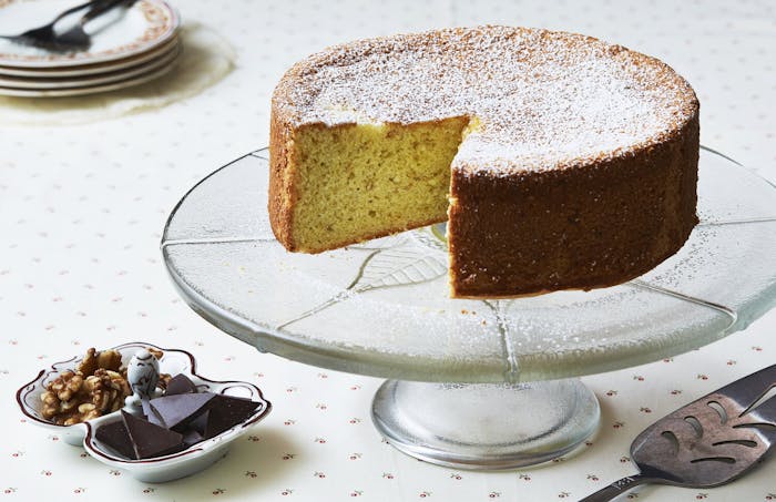 Biscuit on cake tray with slice removed, dish with walnuts and chocolate.