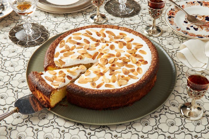 Almond cake with icing and toasted almonds, red wine and serving plates.