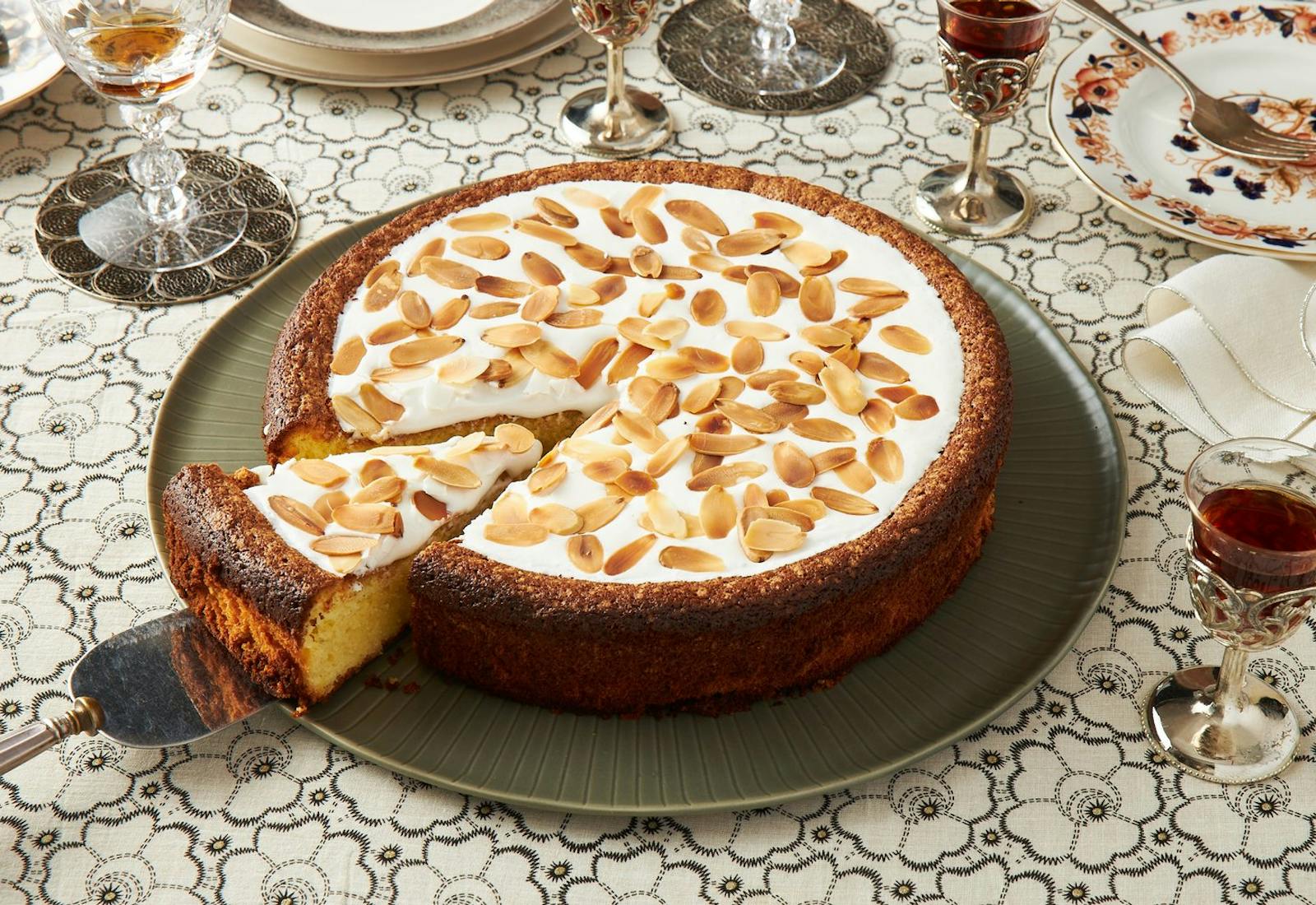 Almond cake with icing and toasted almonds, red wine and serving plates.