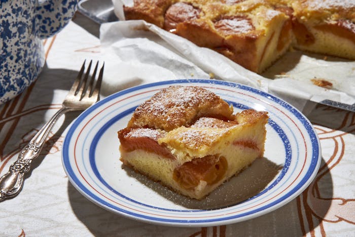 Slice of apricot cake on red and blue striped plate alongside whole cake on pan.