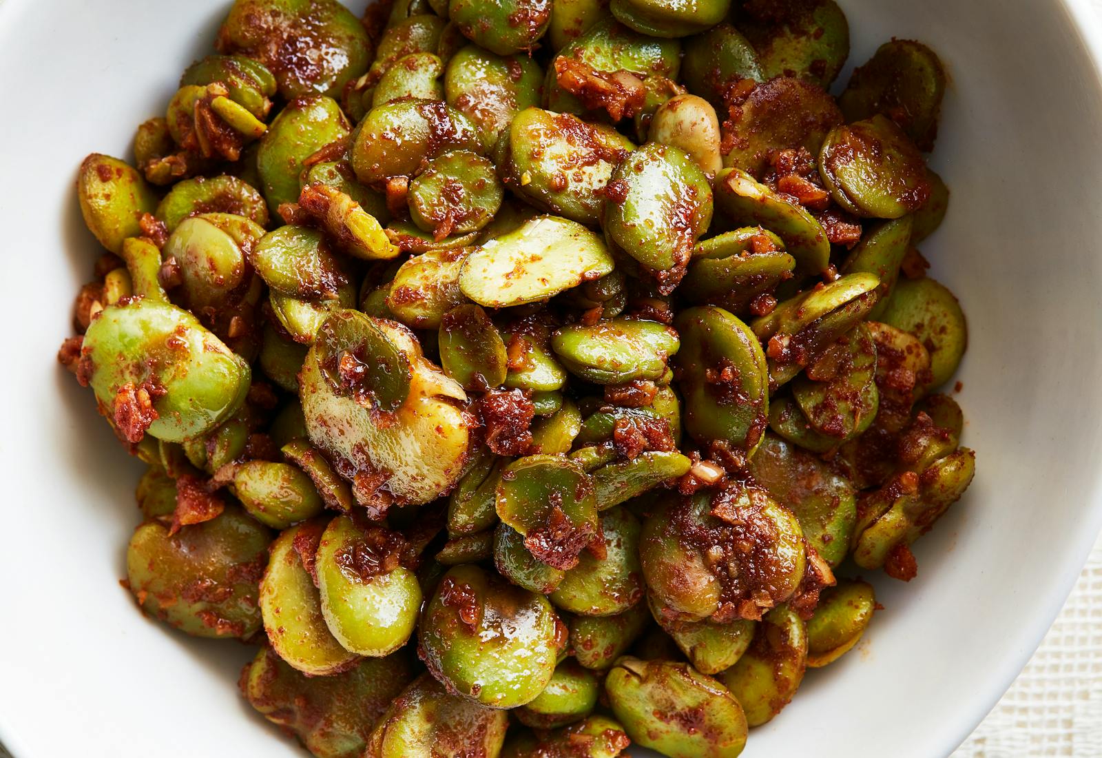 Sauteed fava beans coated in spices in white bowl.