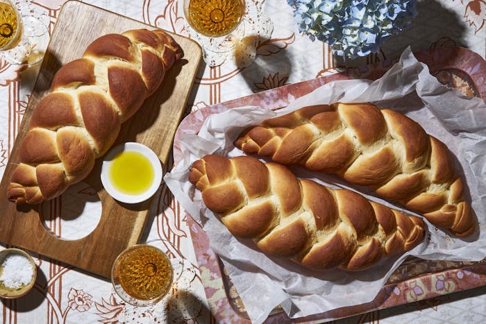 Three loaves of water challah with dishes of maple syrup and coarse salt, glasses of white wine, and fresh flowers.